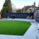 A modern garden patio with artificial grass and pleached tree screening